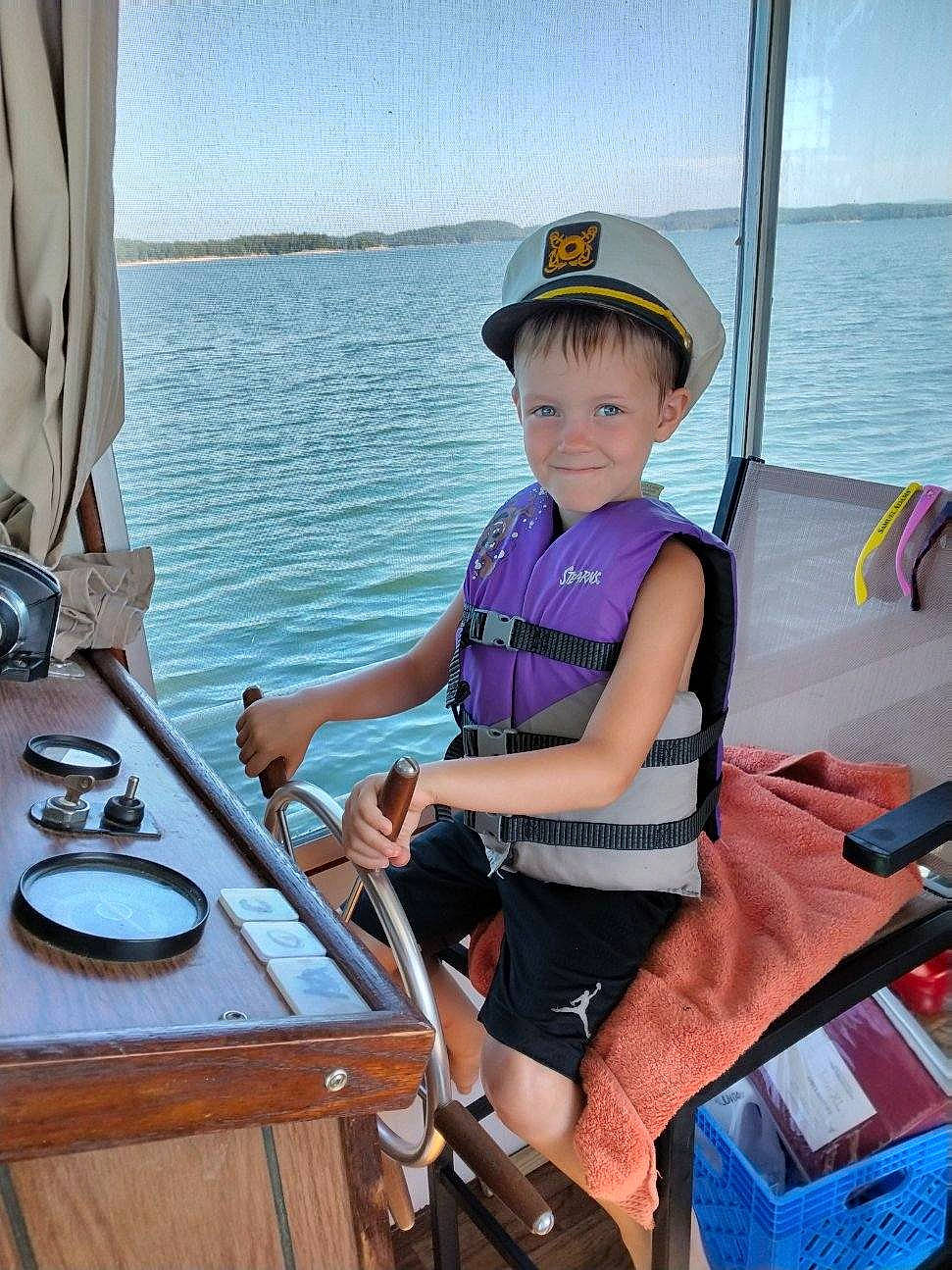 Kaine is registered to the contest to win money with this photo: blue, boat, boats_and_boating_equipment_and_supplies, fun, hat, joy, lake, leisure, naval_architecture, outdoor_recreation, person, recreation, shorts, sky, summer, toddler, travel, vehicle, water, water_transportation