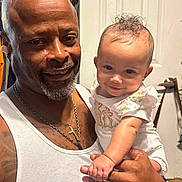 Jolynn joined the competition — help win amazing prizes! baby, infant, child, adult, father, parent, portrait, smiling, indoors, bathroom, holding, family, man, person, curly_hair, floral_clothing, white_shirt, tattoo, necklace, watch