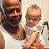 baby, infant, child, adult, father, parent, portrait, smiling, indoors, bathroom, holding, family, man, person, curly_hair, floral_clothing, white_shirt, tattoo, necklace, watch