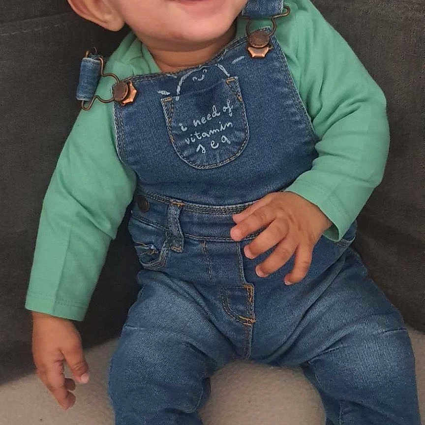 Ylies a rejoint le concours — aidez-le/la à gagner de superbes lots ! baby, casual_clothing, child, couch, cute, denim_overalls, fabric, footwear, green_shirt, happy, indoor, infant, person, playful, portrait, sitting, smiling, socks, white_shoes, young_child