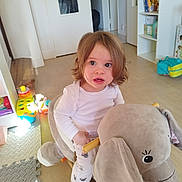 Lucie participe au concours pour gagner de l'argent avec cette photo : backpack, bookshelf, child, clothing, curious, elephant, expression, floor, furniture, home, indoor, light, patterned_pants, playroom, plush, sitting, toddler, toy, white_shirt, wooden_handle