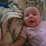 Amy joined the competition — help win amazing prizes! baby, infant, smile, happy, blanket, striped_clothing, flower_emblem, lying_down, cozy, soft_texture, rainbow_pattern, child, cute, skin, face, arm, hand, indoors, comfort, person