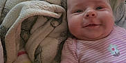 Amy is registered to the contest to win money with this photo: baby, child, smile, face, blanket, soft, cozy, pink_striped_onesie, flower_print, infant, lying_down, cheeks, warm, comfort, couch, fabric, pattern, colorful, rainbow, happy