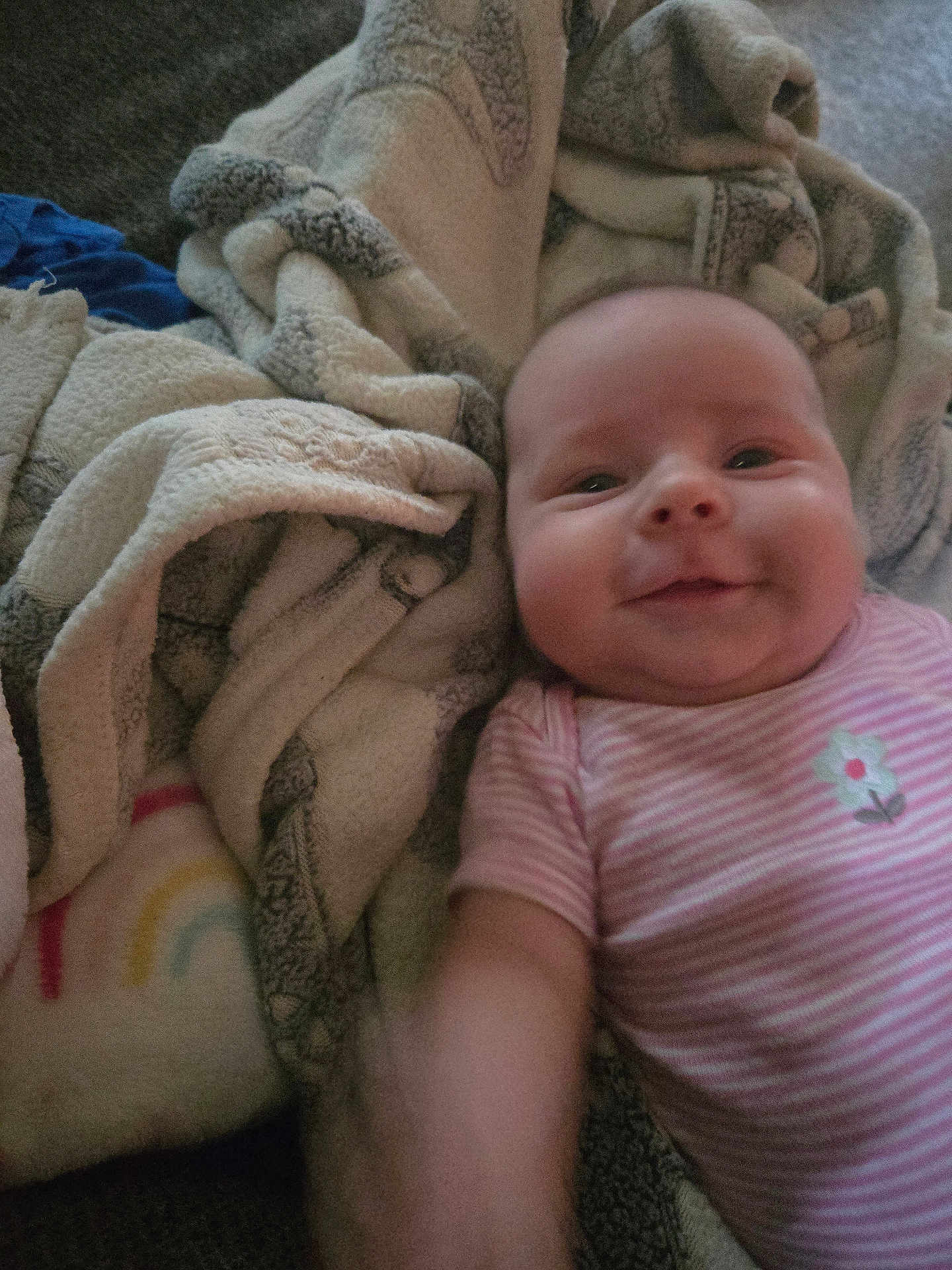 Amy is registered to the contest to win money with this photo: baby, child, smile, face, blanket, soft, cozy, pink_striped_onesie, flower_print, infant, lying_down, cheeks, warm, comfort, couch, fabric, pattern, colorful, rainbow, happy