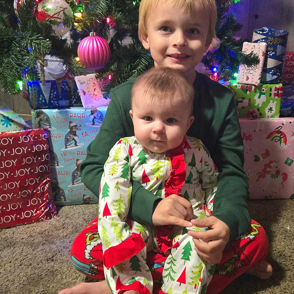 Amy is registered to the contest to win money with this photo: baby, carpet, child, christmas_lights, christmas_ornaments, christmas_tree, family_moment, festive, holiday, holiday_pajamas, indoors, ornament, pajamas, portrait, presents, sibling, sitting, smiling, wrapped_gifts, young_child