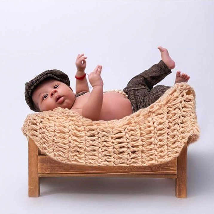 Xander is registered to the contest to win money with this photo: baby, bare_chest, bed, cap, child, curious, cute, feet, hands, indoors, infant, knitted_blanket, lying_down, newborn, pants, portrait, small_bed, studio, white_background, wooden_furniture