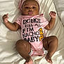 Raine is registered to the contest to win money with this photo: arms_up, baby, child, chubby_cheeks, clothing, cute, head_wrap, humorous_text, indoor, infant, legs_bent, lying_down, nacho_chips, person, pink_onesie, portrait, resting, sleepwear, soft_fabric, white_bed
