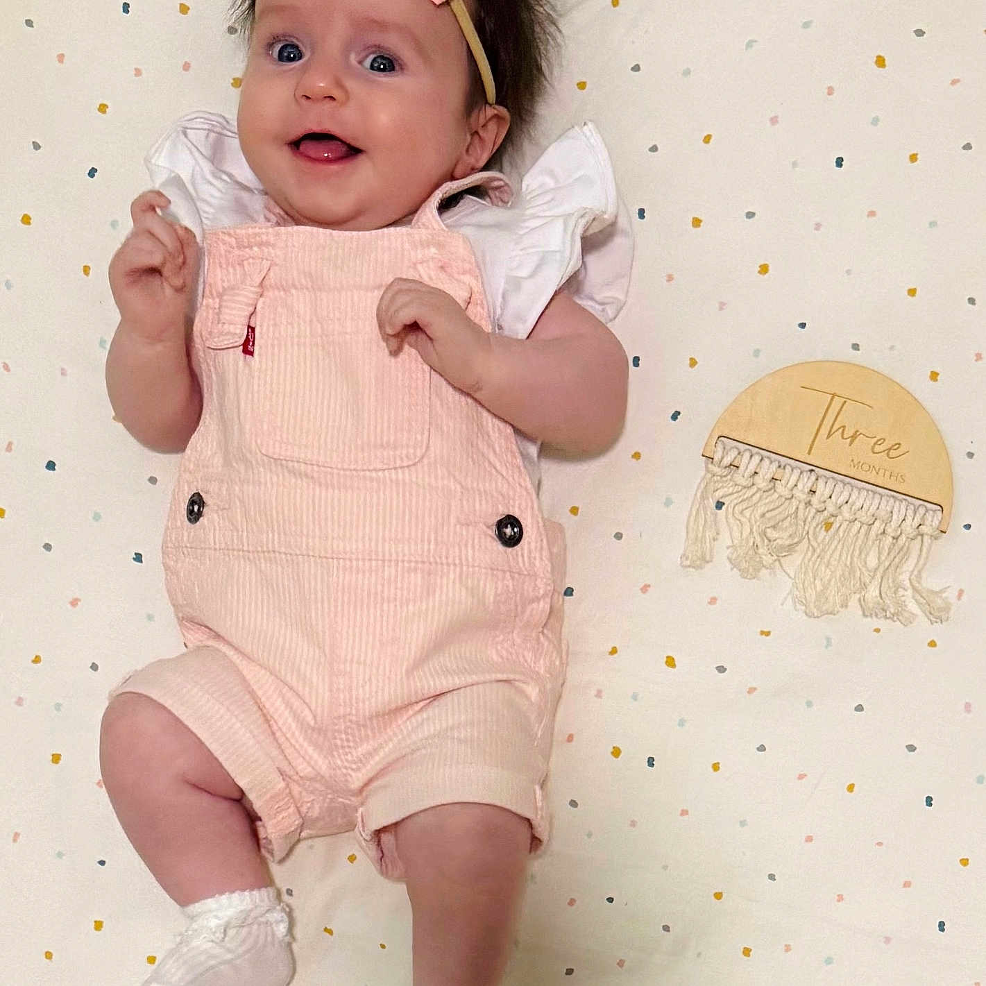 Lily Grace is registered to the contest to win money with this photo: baby, infant, girl, smiling, pink_overalls, headband, bow, white_shirt, socks, milestone, three_months, blanket, polka_dots, macrame, wooden_plaque, cute, lying_down, happy, portrait, child