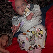 Alexis is registered to the contest to win money with this photo: baby, infant, headband, pajamas, mickey_mouse, minnie_mouse, hand, blanket, red, patterned_background, clothing, cute, lying_down, reaching, adult_hand, indoors, soft_toys, sleepwear, child, person