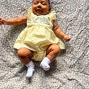 Soraya joined the competition — help win amazing prizes! baby, child, smile, yellow_dress, headband, bow, socks, lying_down, floral_blanket, infant, cute, happy, indoors, portrait, young_child, skin, person, one_person, casual_clothing, baby_girl