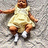 baby, child, smile, yellow_dress, headband, bow, socks, lying_down, floral_blanket, infant, cute, happy, indoors, portrait, young_child, skin, person, one_person, casual_clothing, baby_girl