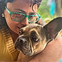 person, dog, french_bulldog, glasses, hug, close_up, face, ear, pet, love, affection, outdoor, natural_light, skin, watch, yellow_clothing, short_hair, brown_dog, portrait, candid