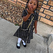 Zyani is registered to the contest to win money with this photo: child, girl, outdoor, dress, black_dress, white_tights, black_shoes, purse, braids, beads, sidewalk, stone_wall, rocks, posing, smiling, cute, fashion, person, young, portrait