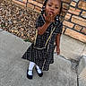 child, girl, outdoor, dress, black_dress, white_tights, black_shoes, purse, braids, beads, sidewalk, stone_wall, rocks, posing, smiling, cute, fashion, person, young, portrait