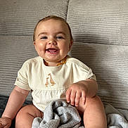 Maéna a rejoint le concours — aidez-le/la à gagner de superbes lots ! baby, smiling, couch, blanket, onesie, beaded_necklace, happy, child, indoor, infant, cute, portrait, sitting, cozy, soft_texture, furniture, face, hand, toe, skin