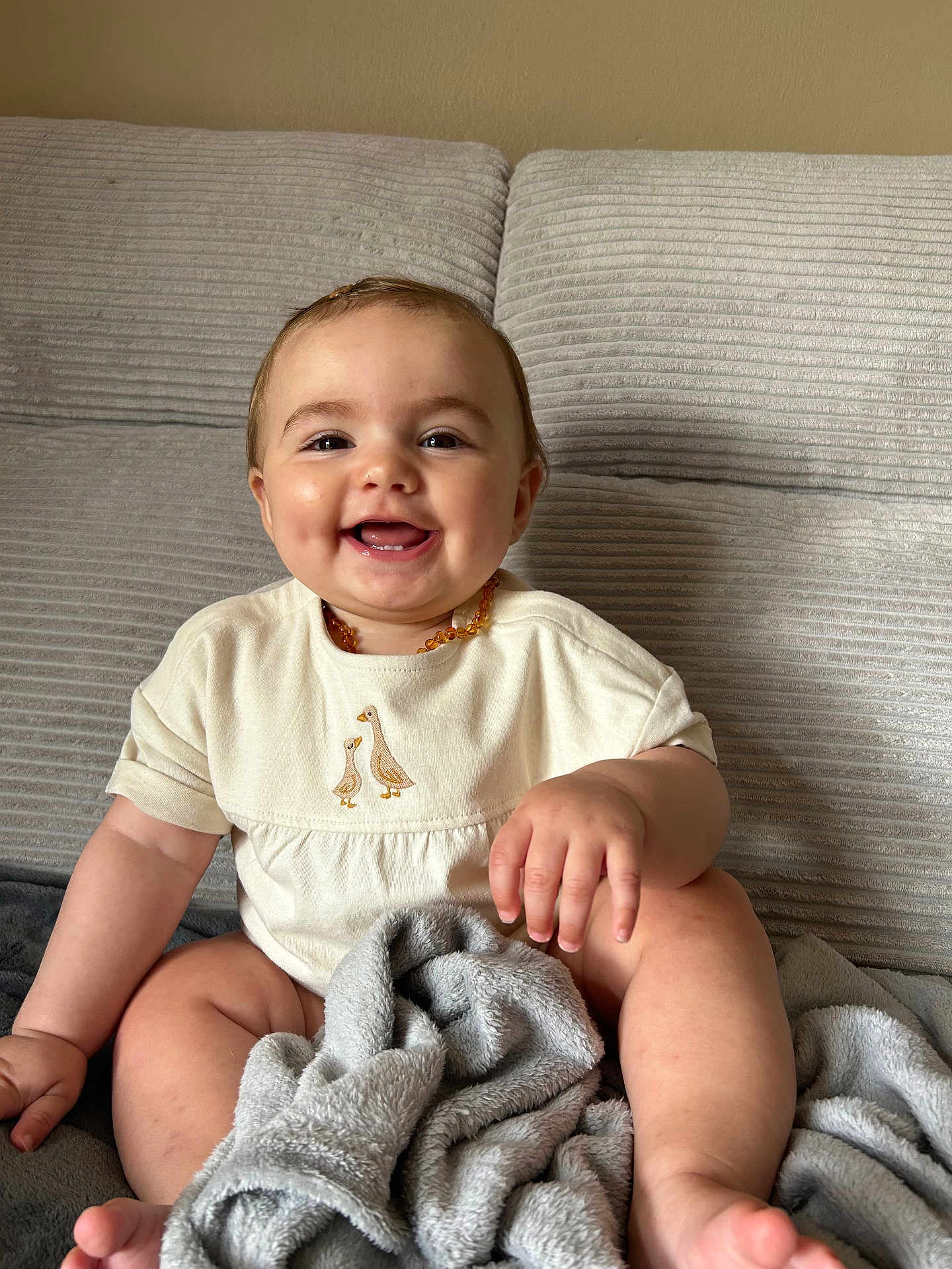 Maéna a rejoint le concours — aidez-le/la à gagner de superbes lots ! baby, smiling, couch, blanket, onesie, beaded_necklace, happy, child, indoor, infant, cute, portrait, sitting, cozy, soft_texture, furniture, face, hand, toe, skin