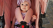 Alana joined the competition — help win amazing prizes! baby, child, stroller, pink, headband, bow, infant, seated, safety_harness, dress, floral_pattern, cute, indoors, carriage, person, portrait, wide_eyes, curious, soft_lighting, baby_clothing