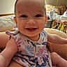 Alana is registered to the contest to win money with this photo: baby, smiling, child, indoor, dress, floral_pattern, person, lamp, couch, furniture, happy, cute, portrait, skin, head, arm, hand, seated, household_items, infant
