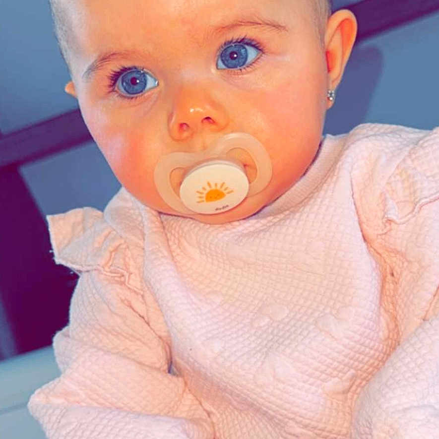 Zoony a rejoint le concours — aidez-le/la à gagner de superbes lots ! baby, child, pacifier, blue_eyes, pink_clothing, bow, indoor, portrait, cute, infant, sitting, young_child, face, hand, soft_texture, clothing, head_accessory, closeup, skin, human