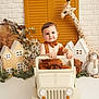 toddler, toy_jeep, bow_tie, suspenders, plush_giraffe, stuffed_toy, miniature_house, decor, child, smile, indoor, playful, cute, white_floor, brick_wall, orange, brown, greenery, photography, portrait