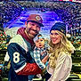 family, baby, man, woman, stadium, hockey_rink, crowd, sports_fans, baseball_cap, beanie, smile, glasses, jersey, stadium_seats, ice, scoreboard, arena_lighting, portrait, hands, beverage_can