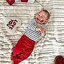 baby, infant, smiling, kiss_marks, striped_shirt, red_pants, blanket, heart_pillow, xoxo_blocks, valentine_theme, cozy, plush, lying_down, bare_feet, joyful, cheeks, white_background, blanket_texture, portrait, holiday_prop