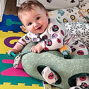 Matéo a rejoint le concours — aidez-le/la à gagner de superbes lots ! animal_print, baby, child, childhood, colorful_mats, cushion, cute, face, floor_mat, happy, home, indoor, infant, pajamas, person, pillow, playful, plush_toy, smiling, toy