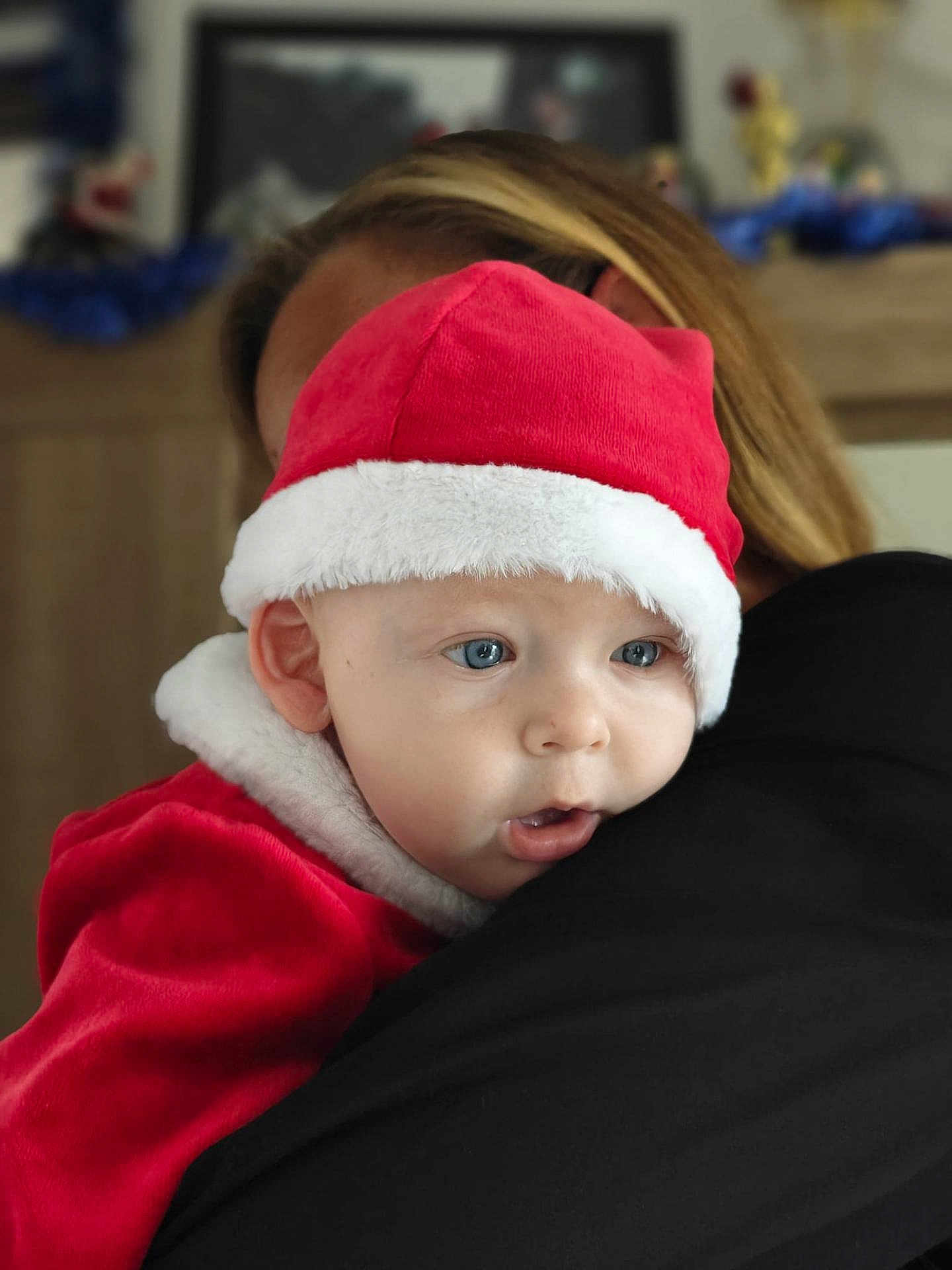 Maxence participe au concours pour gagner de l'argent avec cette photo : baby, child, santa_hat, red_clothing, white_fur_trim, blue_eyes, holding, embrace, indoor, portrait, holiday, festive, person, face, closeup, cute, warm, soft_light, blond_hair, expression
