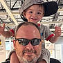 child, toddler, man, beard, sunglasses, hat, cap, smile, happy, shoulders, indoor, store, industrial_ceiling, person, clothing, adult, joy, fun, family, portrait