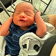 Yadiel is registered to the contest to win money with this photo: newborn, baby, infant, sleeping, smiling, portrait, face, child, blue_outfit, striped_clothing, blanket, stroller, indoor, tiled_floor, arms_up, cozy, parent, tattoo, close_up, family