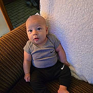 Kaysin joined the competition — help win amazing prizes! baby, infant, child, couch, clothing, grey_shirt, black_pants, nike_logo, sitting, indoors, footwear_absent, patterned_fabric, curious_expression, looking_up, barefoot, soft_blanket, home_interior, wooden_furniture, carpeted_floor, portrait