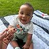 Synceir joined the competition — help win amazing prizes! baby, child, smiling, hand_holding, outdoor, grass, picnic_blanket, tree, greenery, happy, sitting, sock, casual_clothing, person, portrait, nature, daylight, cute, infant, family