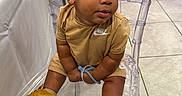 Synceir is registered to the contest to win money with this photo: toddler, child, nike, sneakers, yellow_shoes, tan_clothing, shorts, tshirt, curly_hair, chair, transparent_chair, tile_floor, indoor, person, baby, cute, sitting, looking_away, expression, floor