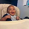 baby, high_chair, bib, smile, happy, food_stains, indoor, child, person, young_child, kitchen, home, mealtime, seat, face, expression, cute, infant, furniture, joy