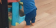 Thymaël participe au concours pour gagner de l'argent avec cette photo : toddler, child, blue_clothing, barefoot, wooden_floor, plastic_table, indoor, toy_scooter, high_chair, standing, back_view, home, flooring, young_child, furniture, person, baby, support, play_area, casual