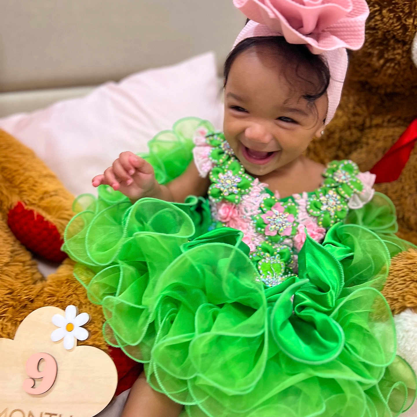 Amirah joined the competition — help win amazing prizes! accessory, baby, bed, celebration, child, cute, fabric, flower, green_dress, happy, headband, indoors, infant, milestone_sign, pillow, plush_toy, portrait, sitting, smiling, teddy_bear
