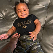 Zákari joined the competition — help win amazing prizes! baby, black_tshirt, camouflage_pants, child, clothing, couch, cute, hair_buns, hand, happy, indoor, infant, leather, person, portrait, relaxing, seated, smiling, tattoo, young_child