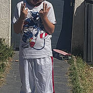 Clement a rejoint le concours — aidez-le/la à gagner de superbes lots ! boy, child, concrete_path, door, fun, gesture, grass, outdoor, pants, playful, shadow, skateboard, sneakers, sonic_the_hedgehog, sunny, tongue_out, tshirt, wall, white_clothing, youth