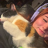 Rumi is registered to the contest to win money with this photo: cat, calico_cat, person, headphones, piercing, nose_ring, black_clothing, indoor, snuggling, sleeping_cat, close_up, pet, relaxation, cozy, fur, face, smile, technology, electronic_device, companion