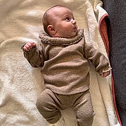 Romy participe au concours pour gagner de l'argent avec cette photo : baby, infant, blanket, knitwear, brown_clothing, socks, face, lying_down, soft_texture, cute, cozy, child, portrait, indoor, newborn, warm_clothing, expression, couch, fabric, relaxed