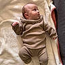 baby, infant, blanket, knitwear, brown_clothing, socks, face, lying_down, soft_texture, cute, cozy, child, portrait, indoor, newborn, warm_clothing, expression, couch, fabric, relaxed