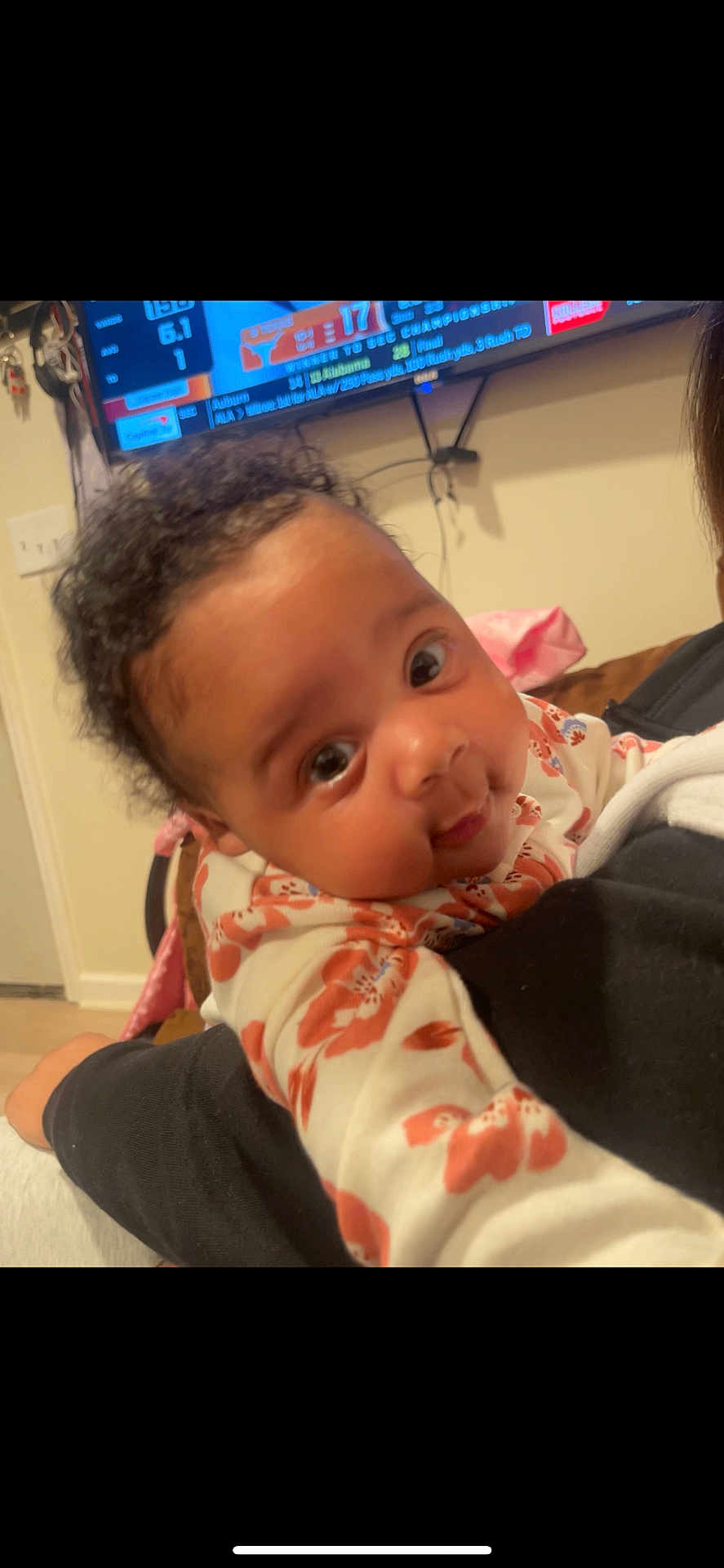 Avionna is registered to the contest to win money with this photo: baby, child, portrait, face, curly_hair, indoor, person, clothing, floral_pattern, hand, arm, television, sports, home, couch, blanket, expression, young, cute, closeup