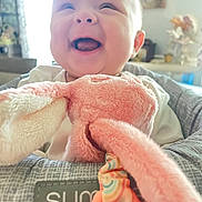 Emilee is registered to the contest to win money with this photo: baby, smiling, infant, toy, stuffed_animal, pink, cushion, indoor, child, happy, face, person, seat, soft, plush, cute, home, portrait, comfort, joy