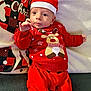 baby, infant, christmas, holiday, festive_clothing, red_outfit, santa_hat, reindeer_sweater, couch, cushion, indoor, portrait, cute, smiling, child, person, holiday_decor, seasonal, cozy, happy