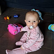 Brice Chretien participe au concours pour gagner de l'argent avec cette photo : baby, pacifier, pink_outfit, toy_car, floor, tiles, child, indoor, cute, smiling, play, toy, sitting, infant, person, young_child, colorful, fun, beads, comfort