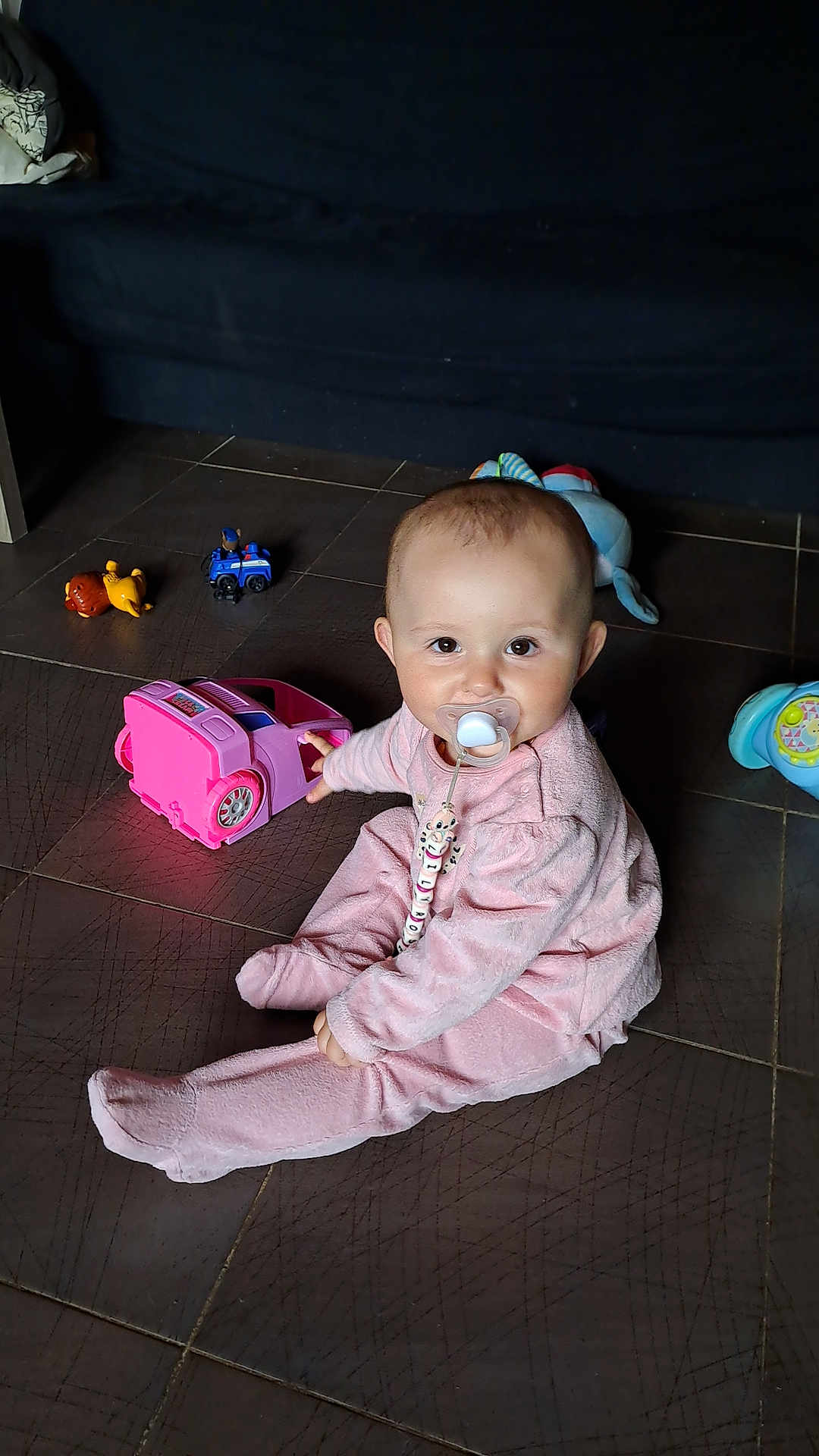 Brice Chretien participe au concours pour gagner de l'argent avec cette photo : baby, pacifier, pink_outfit, toy_car, floor, tiles, child, indoor, cute, smiling, play, toy, sitting, infant, person, young_child, colorful, fun, beads, comfort