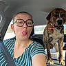 backseat, brindle_fur, car, collar, dog, glasses, happy, interior, outdoor_view, portrait, road_trip, seat_belt, selfie, standing, striped_shirt, sunlight, tongue_out, travel, vehicle, woman
