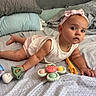 baby, infant, child, bed, pillow, blanket, toy, headband, bow, tummy_time, curious, indoors, soft_lighting, sleeping_area, clothing, person, skin, face, expression, playtime