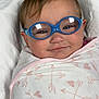 baby, infant, glasses, blue_glasses, swaddle, blanket, pattern, heart_pattern, arrow_pattern, smile, face, head, cute, child, person, eyewear, soft_lighting, indoors, closeup, portrait