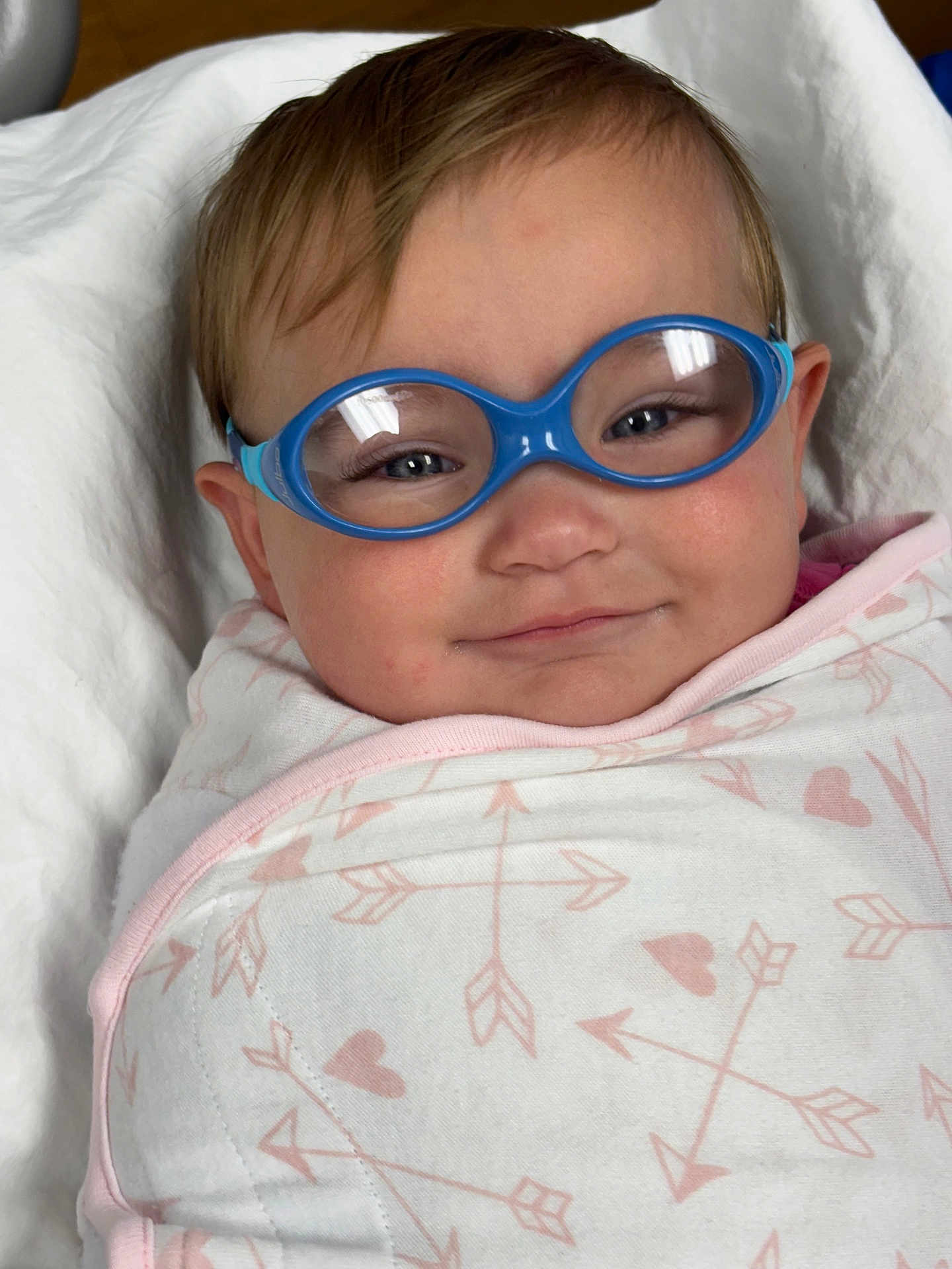 Jaxxon is registered to the contest to win money with this photo: baby, infant, glasses, blue_glasses, swaddle, blanket, pattern, heart_pattern, arrow_pattern, smile, face, head, cute, child, person, eyewear, soft_lighting, indoors, closeup, portrait